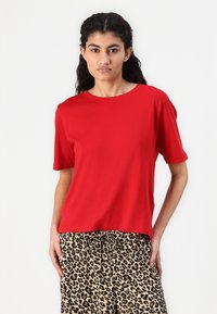 T-shirt rossa a maniche corte con scollatura rotonda, abbinata a pantaloni beige con stampa leopardata. Tessuto morbido, vestibilità comoda e design semplice.