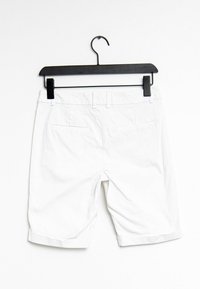 Shorts en coton blancs accrochés à un cintre noir, avec une taille standard, deux poches arrière et des ourlets retroussés pour le détail.