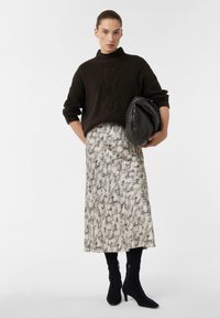 Ciemny sweter w prążki z wysokim kołnierzem, zestawiony z teksturowaną spódnicą do kolan w wzór wężowy oraz czarnymi botkami za kostkę.