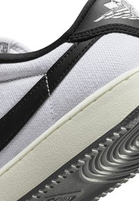 Sneaker bianca in tela con dettagli in pelle nera, suola in gomma testurizzata e design cucito. Presenta un motivo a onda distintivo sulla suola.