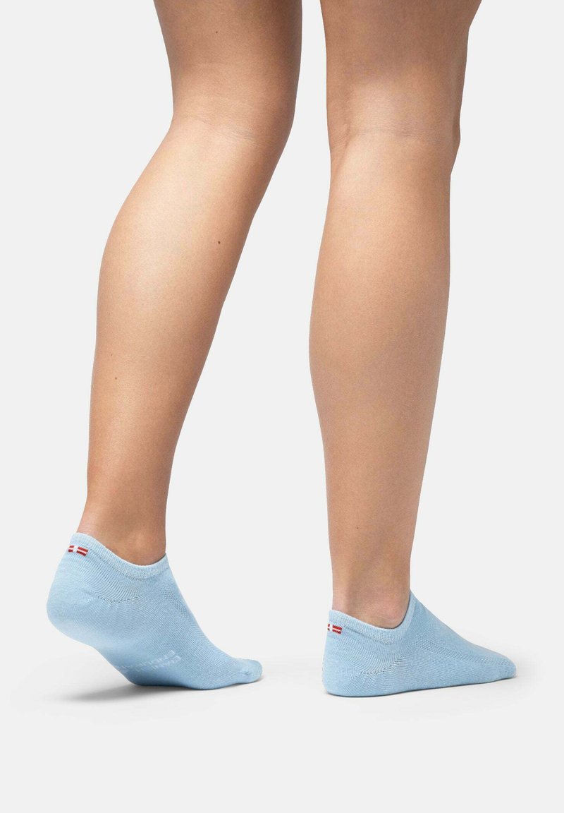 Calzini alla caviglia azzurro chiaro con una texture liscia e accenti rossi e bianchi contrastanti sul tallone, posizionati su una gamba nuda su uno sfondo neutro.