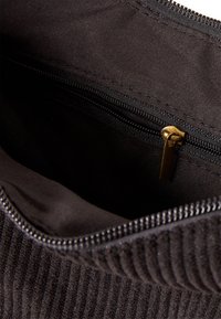 Vnitřek černé látkové tašky s kapsou na zip. Zip má mosaznou táhlo a podšívka má hladkou, matnou texturu.