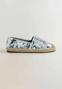Chaussure espadrille à enfiler recouverte de sequins argentés, avec une semelle en jute tressé et un bout arrondi sur fond neutre.
