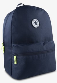 Sac à dos bleu marine en forme arrondie, avec une poche zippée à l'avant, des tirettes de fermeture éclair jaunes et un patch logo circulaire avec un design d'étoile.