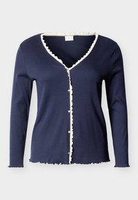 Μακρυμάνικη μπλε ναυτικού καρντιγκάν με λευκή κυματοειδή διακόσμηση κατά μήκος του V-λαιμού, του μπροστινού μέρους με κουμπιά, των μανσετών και του τελειώματος.