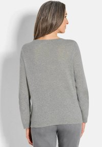 Maglione grigio chiaro con scollo rotondo e maniche lunghe. Tessuto morbido con orlo a coste, indossato sopra pantaloni grigi. Vista posteriore mostrata.