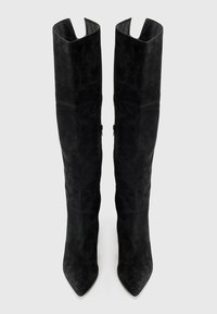 Botas de ante negras hasta la rodilla con puntera afilada y parte superior con muescas. Presentan cremalleras laterales y una textura suave y mate.