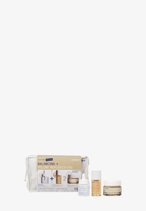 Set di prodotti per la cura della pelle con tre flaconi di crema e siero, etichettati Balancing + Volume Replenishing, esposto davanti a una pochette bianca con zip.