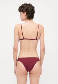 Burgundy bikini set with thin straps and a ribbed texture. The top features adjustable clasps, while the bottom has a classic cut.