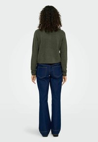 Olivno zeleno skrajšano pulover s okroglim izrezom in dolgimi rokavi, v kombinaciji s temno modrimi flared jeans hlačami, ki imajo zadnje žepke.