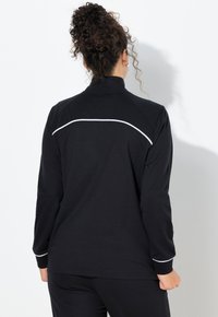 Schwarzes Langarmshirt mit hohem Kragen, das an den Schultern und am Rücken kontrastierende weiße Paspeln aufweist, gefertigt aus einem glatten, elastischen Stoff.