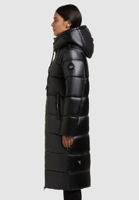 Sort puffer-jakke med en lang, lige silhuet, oversize hætte og vandret quiltet mønster. Har logo-patch på ærmet og forlommer.