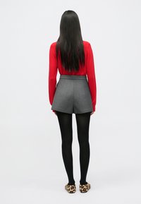 Jersey rojo de manga larga, pantalones cortos grises de talle alto, medias negras y zapatillas con estampado de leopardo. Textura suave y diseño ajustado.