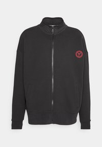 Schwarze Zip-Hoodie mit hohem Kragen, ausgestattet mit einem strukturierten Kragen-Design, seitlichen Taschen und einem roten gestickten Logo auf der linken Brust.