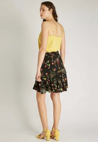 Haut à bretelles jaune associé à une jupe noire à motifs floraux à plusieurs niveaux. La tenue présente une taille cintrée et un ourlet froncé.