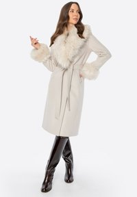 Beżowy wełniany płaszcz z kołnierzem i mankietami z sztucznego futra, z paskiem w talii. Połączony z błyszczącymi, brązowymi botkami do kolan.