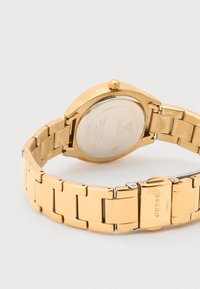 Reloj de pulsera en tono dorado con caja redonda y brazalete metálico texturizado. Presenta una corona prominente y un acabado cepillado en los eslabones del brazalete.