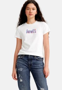 Camiseta blanca de algodón con un logo multicolor de "levi's", combinada con unos vaqueros de mezclilla azul desgastados. Manga corta y escote redondo.