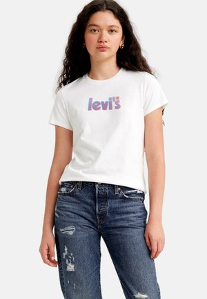 Camiseta blanca de algodón con un logo multicolor de "levi's", combinada con unos vaqueros de mezclilla azul desgastados. Manga corta y escote redondo.