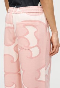 Ροζ βαμβακερές φόρμες με έντονο αφηρημένο σχέδιο, ελαστική μέση και πίσω τσέπη. Λείο ύφασμα, άνετη εφαρμογή.