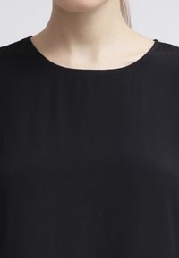 Svart topp i slät tyg med rund halsringning. Har en enkel design och saknar synliga mönster eller detaljer.