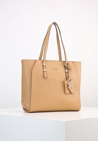 Sac fourre-tout en cuir tan avec doubles poignées, forme structurée, accents en métal argenté et étiquette de porte-clés amovible.
