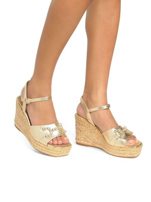 Gouden wig-sandalen met een geweven jute zool. Heeft een crisscross bandontwerp met decoratieve versieringen op de bovenkant. Open teen stijl.