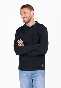 Schwarzes Langarm-Polohemd mit einer Drei-Knopf-Leiste, gerippten Bündchen und Saum sowie einem kleinen Markenetikett auf der linken unteren Seite.