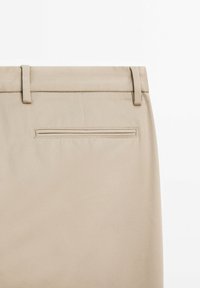 Beige trousers with a textured fabric, featuring belt loops, a back pocket with a horizontal zipper, and clean stitching details.