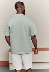 Mintgroen T-shirt met korte mouwen en een ontspannen pasvorm, gecombineerd met lichtgrijze shorts. Gladde katoenstructuur, eenvoudig ontwerp, zonder zichtbare patronen of accenten.