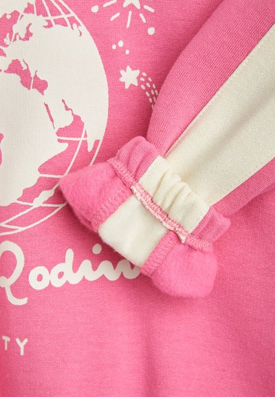 Roza pulover z belim grafičnim motivom zemeljske krogle, s svetlo rožnatim in kremnim mehkim, nabranim manšetom. Tekstura se zdi gladka in udobna.