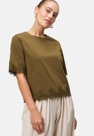 Haut olive en coton doux à manches courtes, avec un bord en dentelle festonnée à l'ourlet. Associé à un pantalon léger plissé.