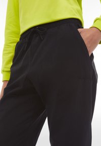 Schwarze Jogginghosen mit einem elastischen Bund und Kordelzug sowie Seitentaschen, kombiniert mit einem leuchtend gelben Langarmshirt.