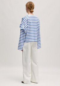 Blauw en wit gestreepte lange mouw top met geplooide schouderdetails, gecombineerd met losse witte broeken. Casual, lichtgewicht katoen.
