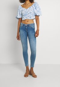 Blusa corta de flores azul claro con mangas abullonadas, combinada con jeans de mezclilla azul medio ajustados y sandalias de tacón bloque en color marrón claro.