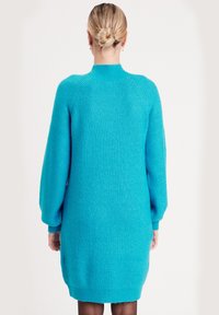 Strickkleid in leuchtendem Türkis, mit Rippstruktur, langen Raglanärmeln, hohem Kragen und einer etwas oversized Passform.