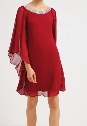Rød chiffon-kjole til knæet med transparente kapperærmer og en perlebesat halsudskæring, båret af en stående person mod en ensfarvet baggrund.