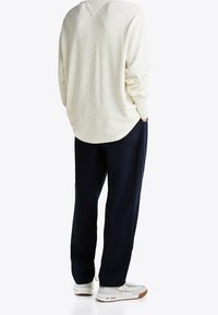 Light cream long-sleeve shirt with textured knit, paired with dark navy pants. White sneakers feature a subtle brown sole detail.