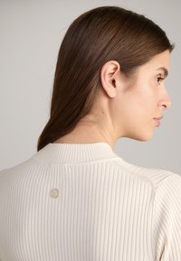 Pull crème côtelé avec un col haut, en tissu texturé, et un petit détail en métal au dos.