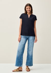 Maglietta navy a maniche corte con scollo a V, abbinata a jeans larghi blu chiaro e sandali marroni. Design semplice, tessuto dalla consistenza liscia.