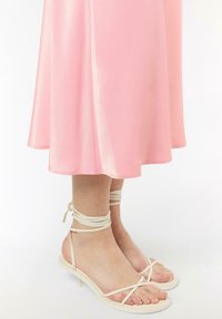 Różowa satynowa sukienka o zwiewnym fasonie, połączona z jasnobeżowymi sandałami na cienkim obcasie i z zawiązaną szyjką.