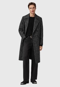 Grå, struktureret lang frakke med dobbeltradet design, parret med en sort ribbet sweater og sort brede bukser. Sort bælte og sko.