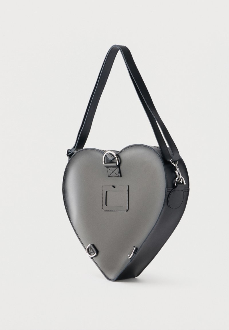 Black heart-shaped handbag with adjustable strap and metal rings, displayed against a plain light background.