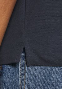 T-shirt en coton bleu marine avec une fente sur le côté, associé à un jean en denim bleu clair. Le tissu présente un tissage texturé et des détails cousus.