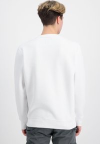 Hvid sweatshirt med lange ærmer og rund hals, med en firkantet mærkedetalje på bagsiden og ribbede manchetter og kant.