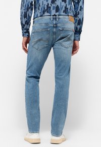 Svetlomodré denim nohavice majú rovný strih, dve zadné vrecká s trojuholníkovým prešitím a koženú nášivku so značkou na páse.
