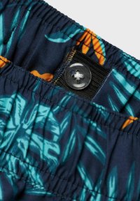 Pantalones cortos azul marino con un patrón botánico que presenta hojas en tono teal y acentos naranjas. Incluyen una cintura elástica y cierre de botón.