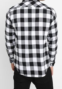 Zwart-wit geruit flanellen overhemd met lange mouwen, een kraag en knoopsluiting. Zachte textuur met contrasterende patronen.