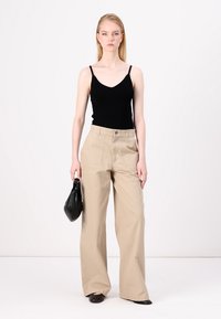 Svart ribbet tanktopp, lysebeige vide bukser med frontlommer, og svart håndveske. Enkelt design, myk tekstur, nøytral fargepalett.