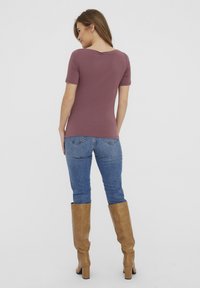 Korte ermers, mauve tettskjorte med vid halslinje. Kombinert med blå jeans og knelang beige støvler med en glatt tekstur.